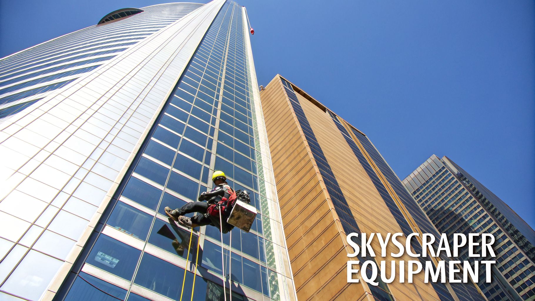 A person in safety gear rappels down a modern glass skyscraper, likely washing windows.
