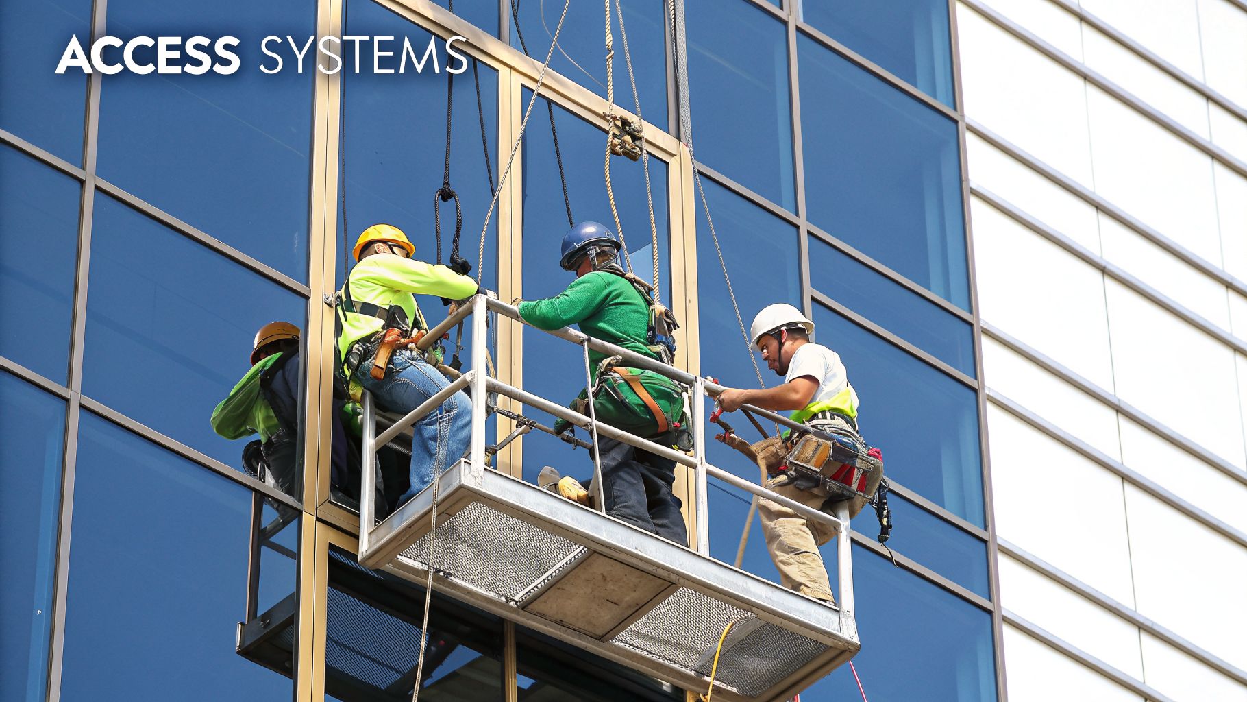 Three workers in safety gear on a suspended platform clean high-rise windows, utilizing access systems.