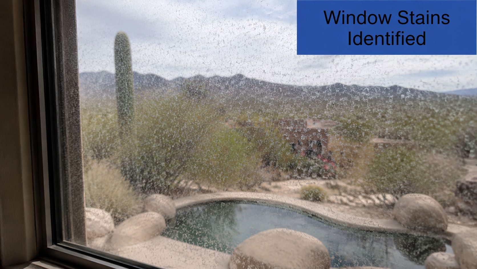 A dirty window covered in white mineral deposits and water spots looking out over a desert landscape.
